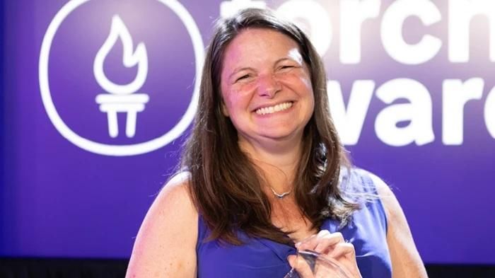 Dawn Laney standing with the TORCH Awards logo in the background holding her award.