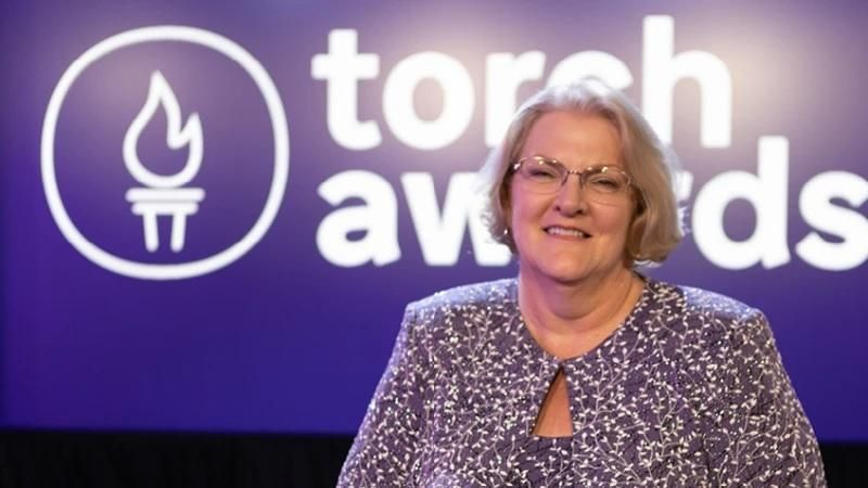 Terri Klein standing with the TORCH Awards logo in the background.