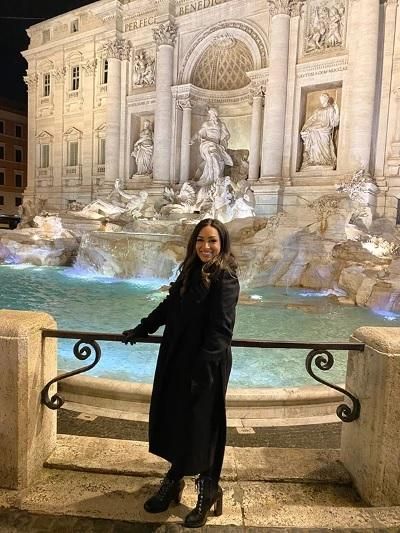 Melissa stands in front of the Trevi Fountain in Rome at night, smiling at the camera.