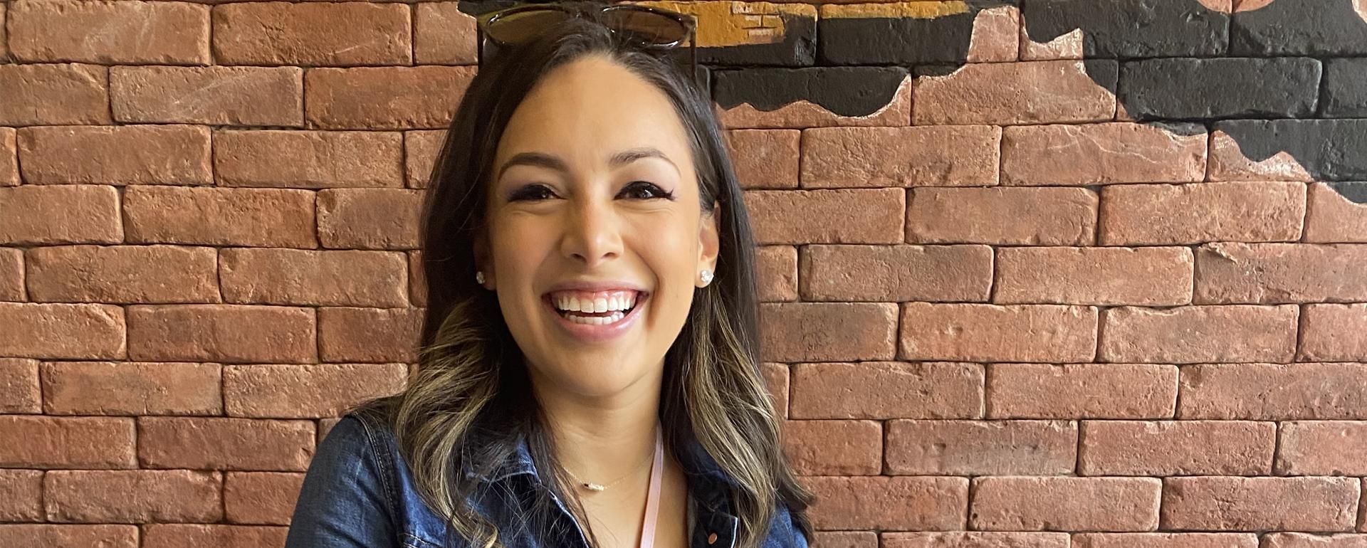 Melissa Aguilar smiles at the camera with a brick wall behind her.