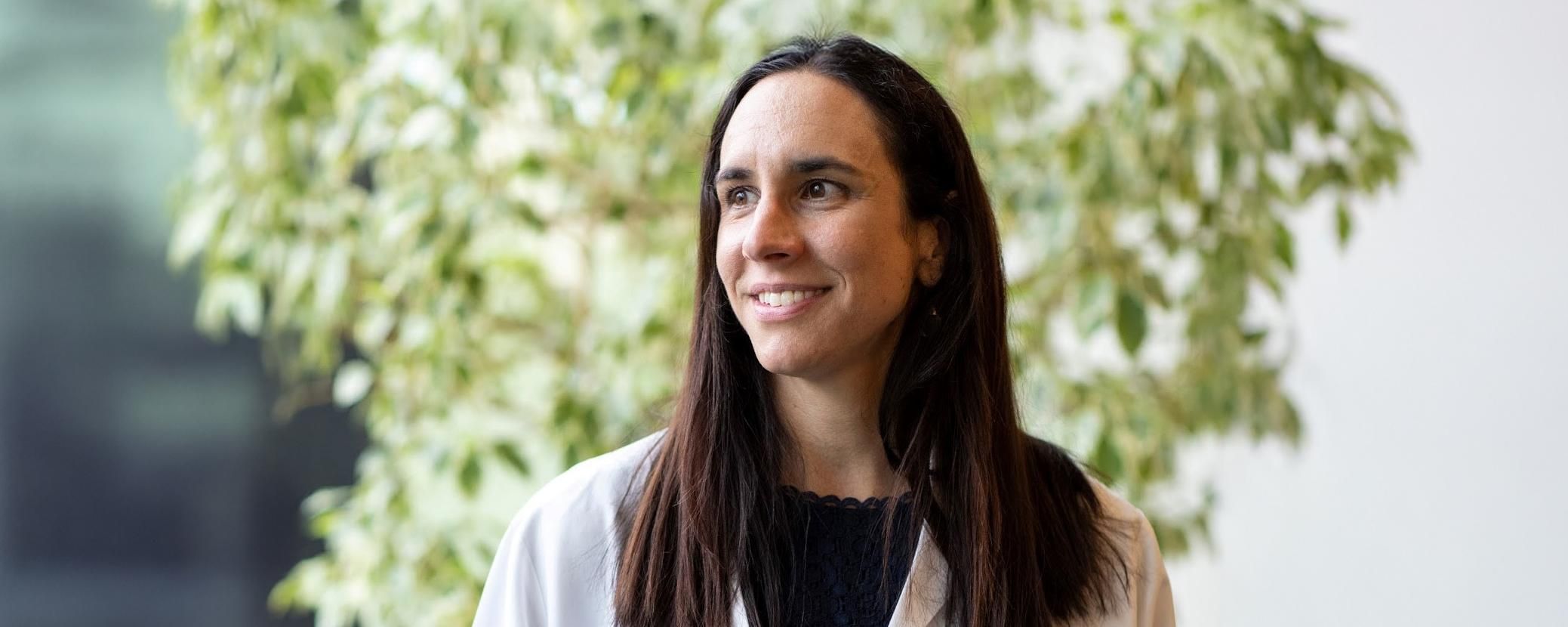 Dr. Katie Sharff smiling and looking off to the side in a white coat against a nature background
