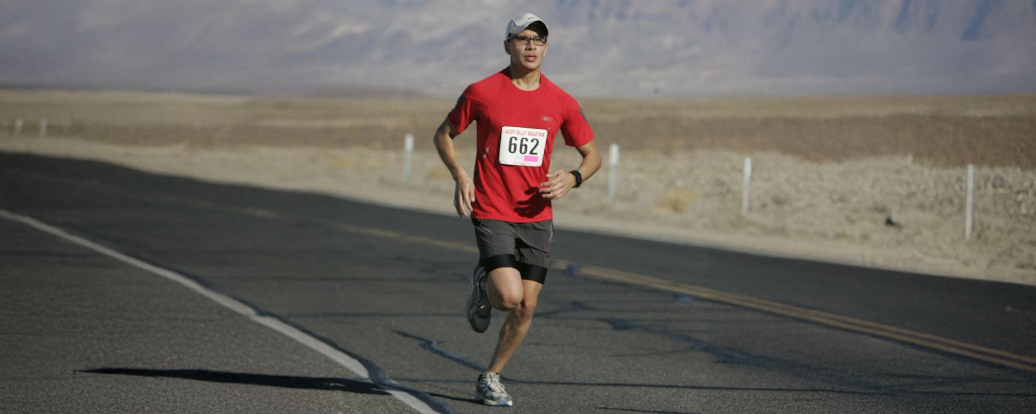 Patient living with Hemophilia A running a half marathon on a desert road. He is wearing a red t-shirt and dark grey shorts and has the race number 662 on his shirt front.