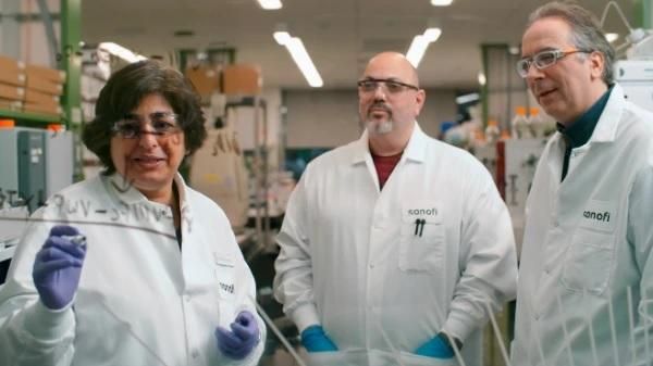 Ekta Seth Chhabra writes on a clear dry erase board whicle two male scientists look on.