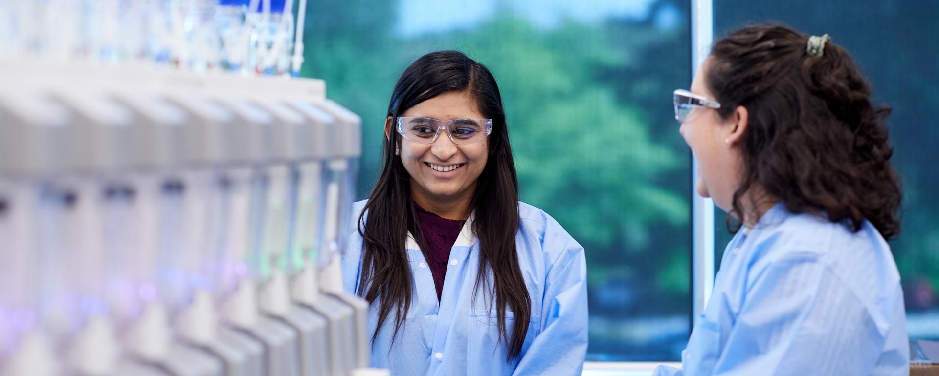 Two female Sanofi scientists in the lab laugh with each other as they perform tests. 