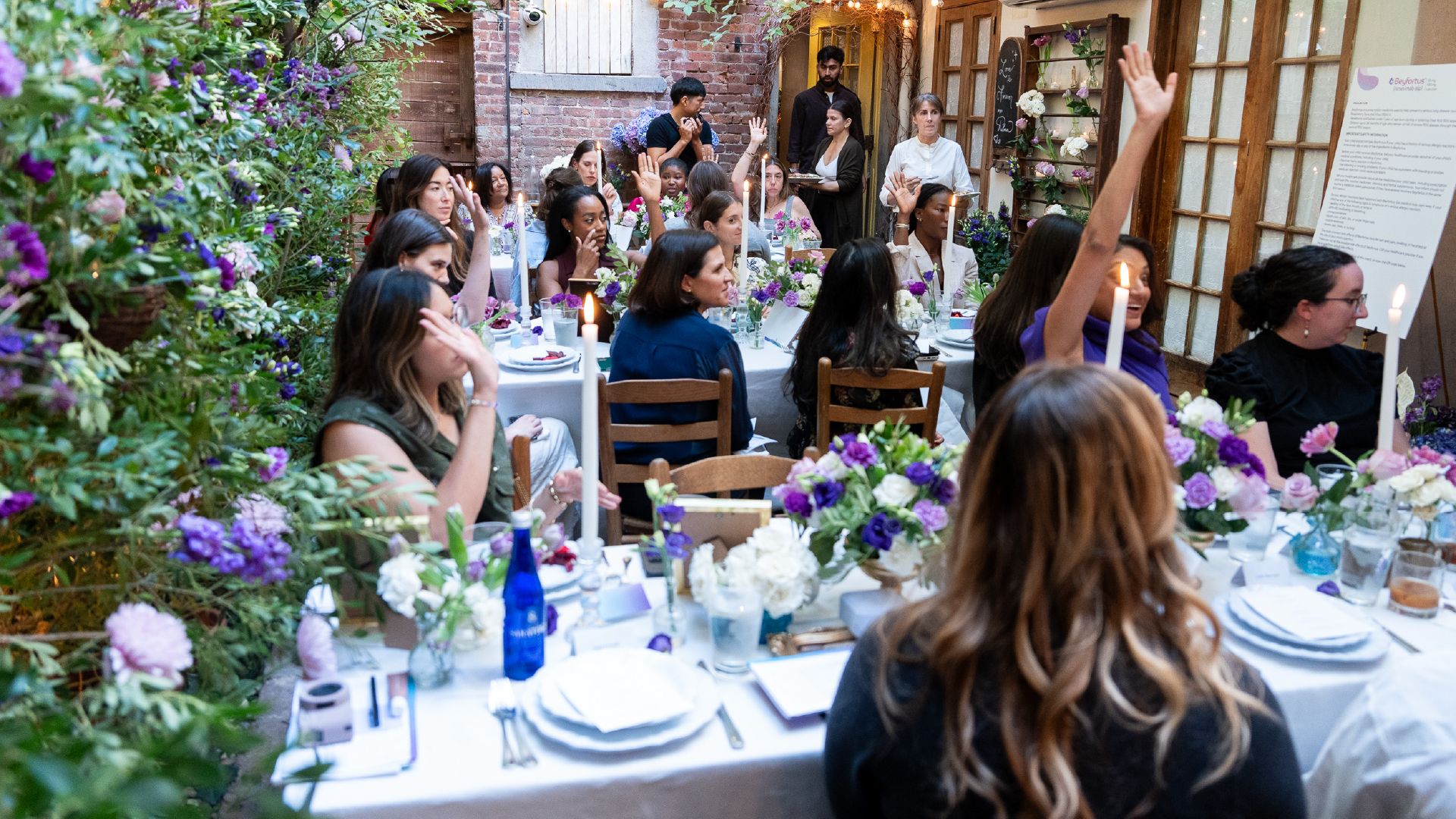 guests sit at lunch table, some with raised hands