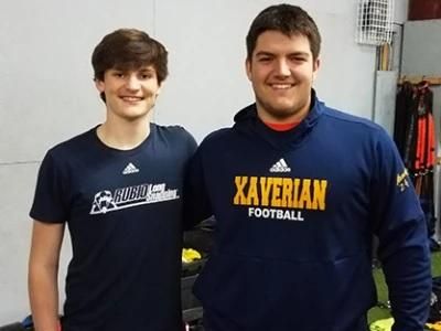Andrew and Jay stand next to each other smiling wearing t-shirts with their high school logos.