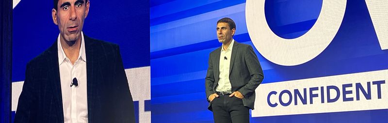 Man dressed a suit presenting in front of screen.