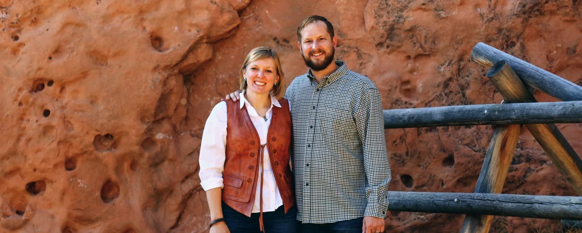 Melanie Stutts stands with her arm around her husband against a stone wall backdrop in Arizona.