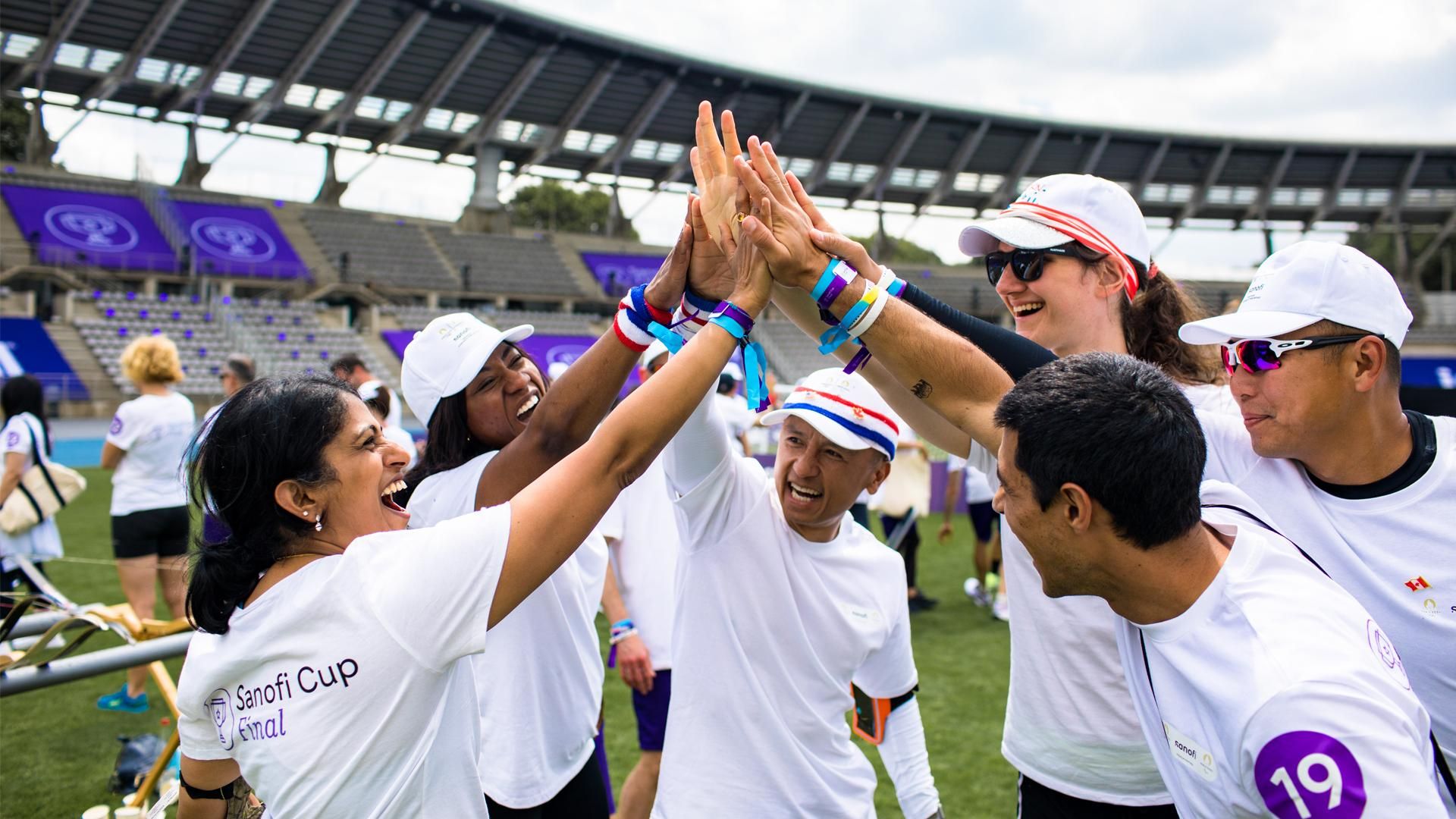 The North America Sanofi Cup team stands in a circle giving each other a group high five.