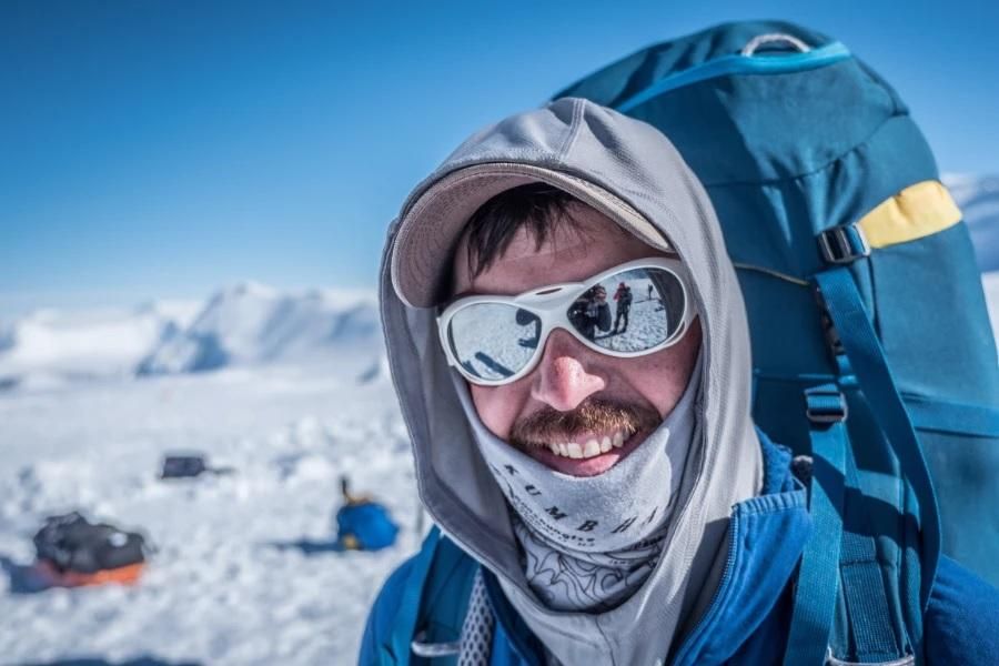 A man dressed for cold weather stands on a snow-covered mountain.