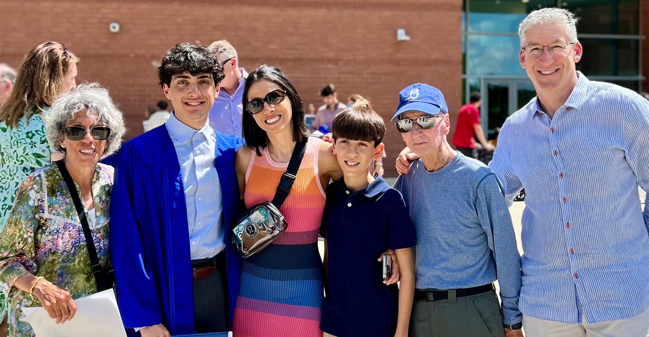 Lew standing arm in arm with five members of his family at his grandson’s graduation.
