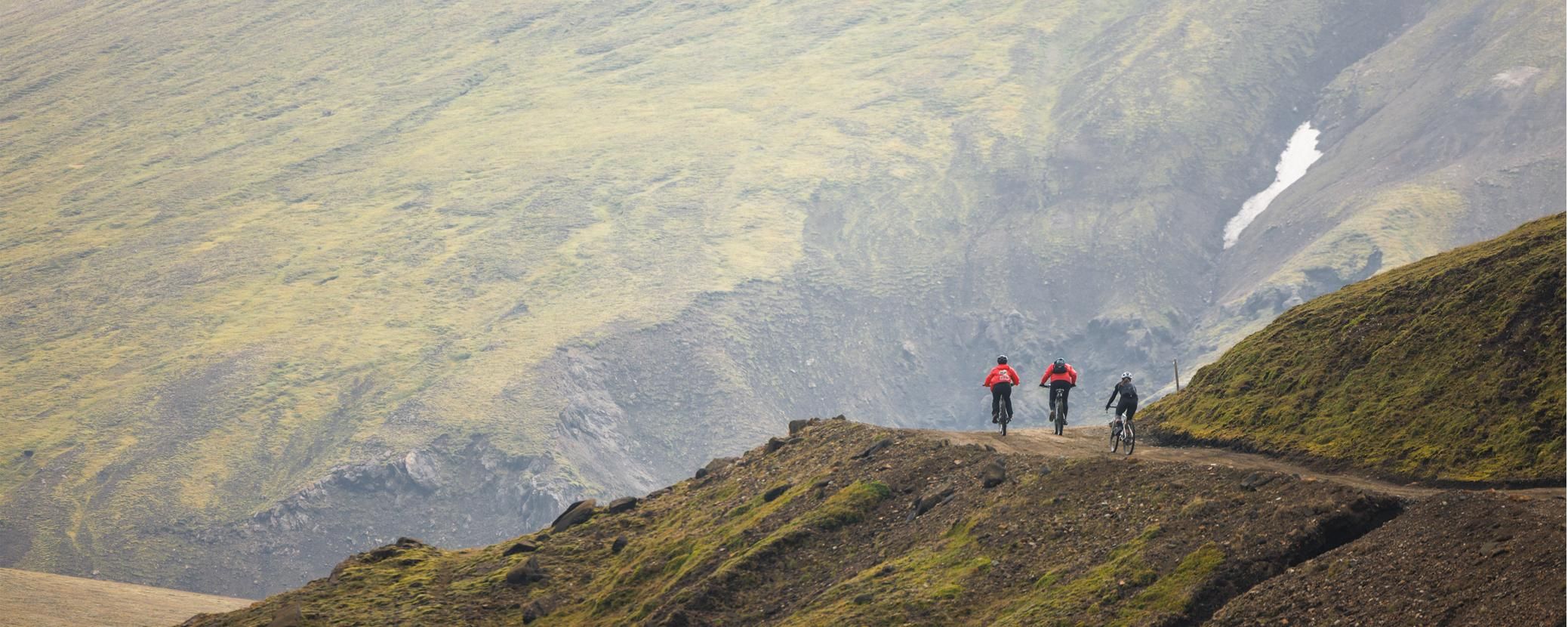 Three cyclists riding along a mountainous path.