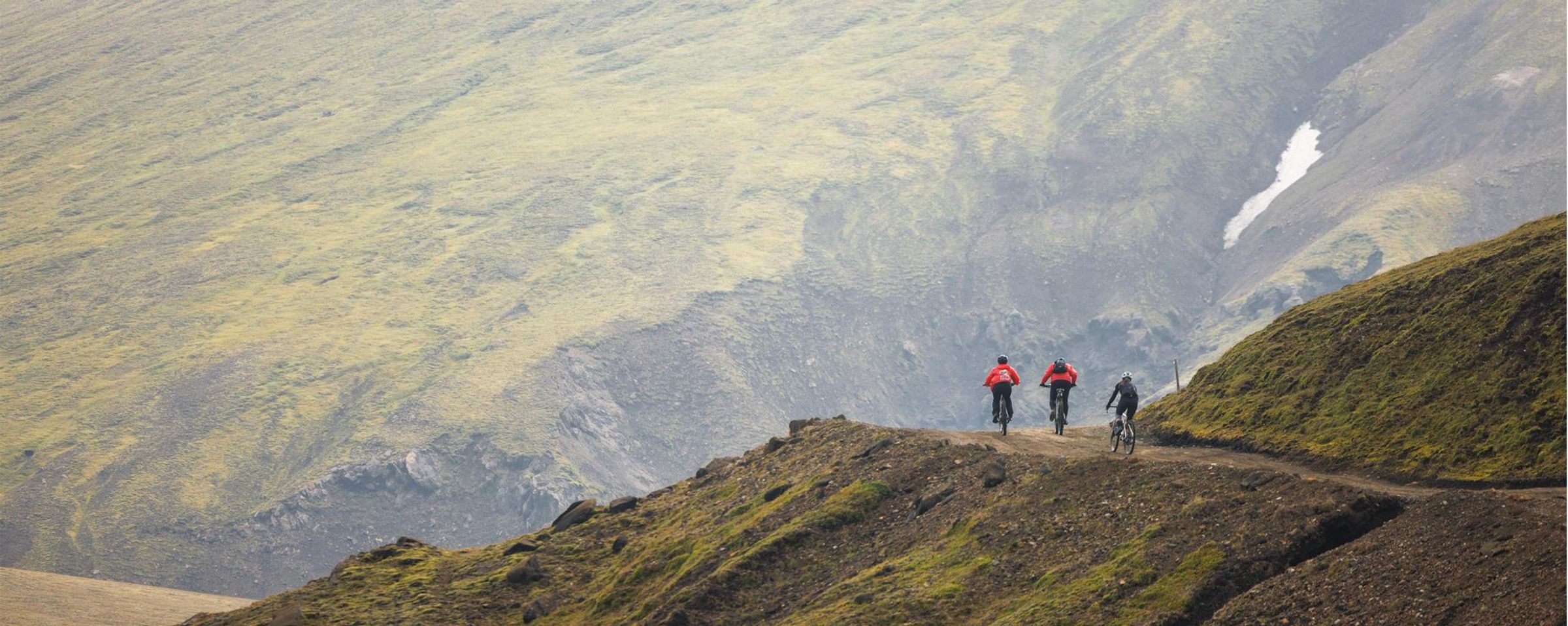 Three cyclists riding along a mountainous path.
