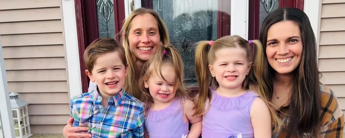 Amy sits on the front stoop of her home on a spring afternoon with her wife and their three children