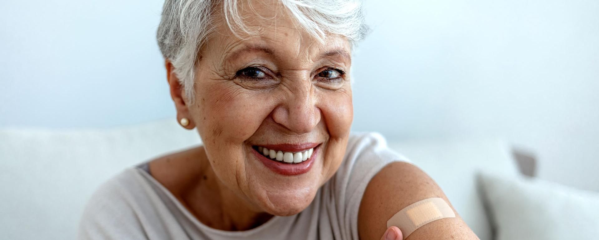 An older woman shows off her arm with  bangage from getting her flu shot.