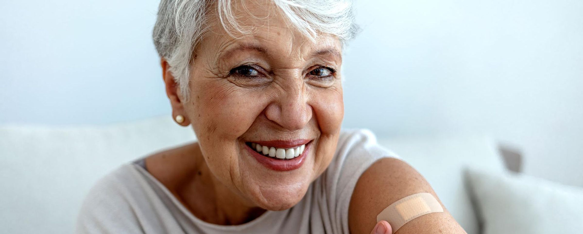 An older woman shows off her arm with bangage from getting her flu shot.