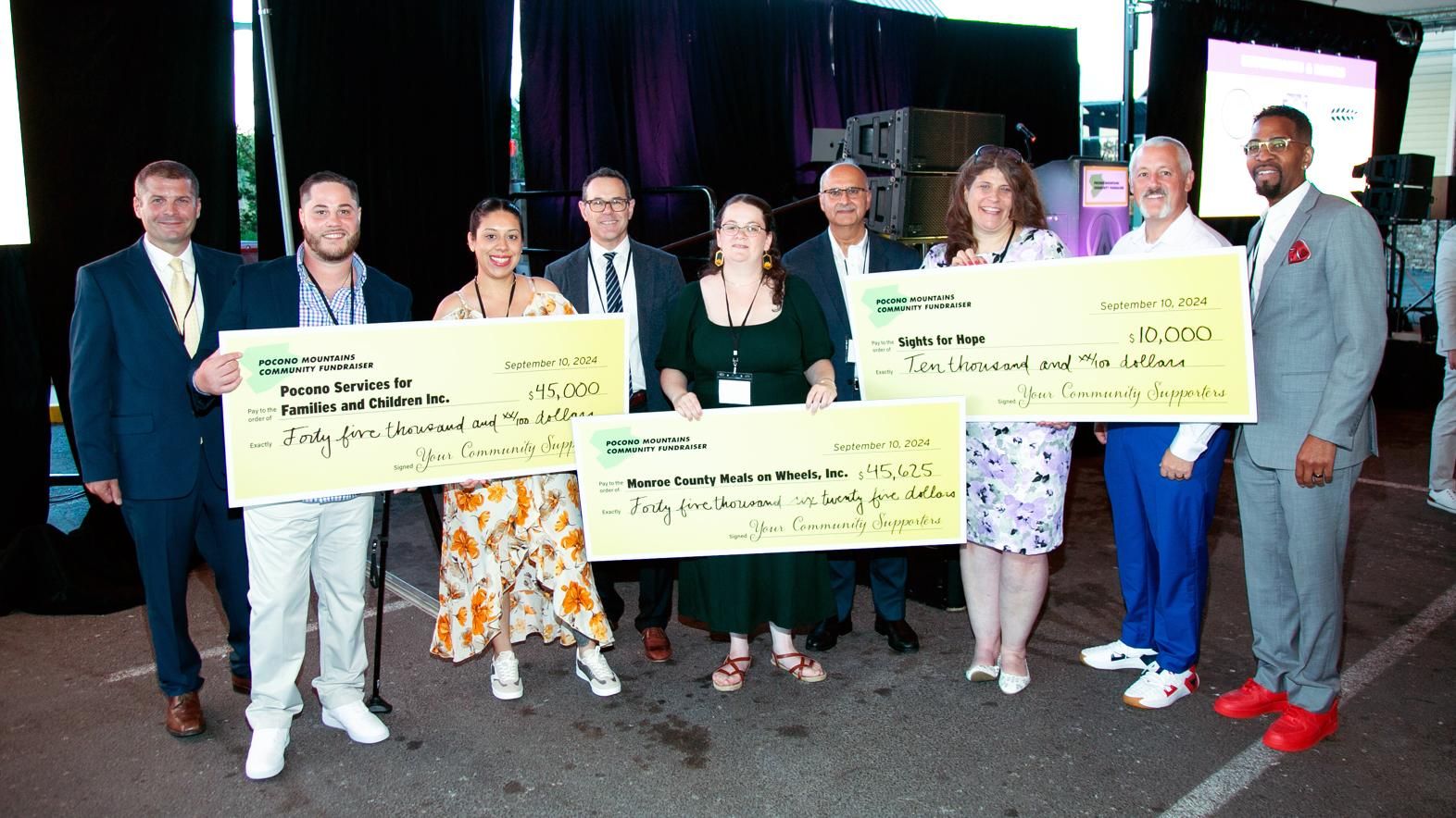 Sanofi employees and members of the Pocono Mountains Community Fundraiser poise for a picture holding three large, posterboard checks totaling over $100,000 for non-profit organizations in the area