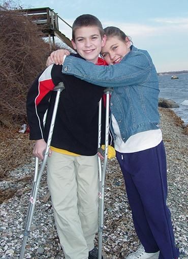 Leland Smith stands on crutches as his sister Taylor Smith wraps her arms around him.