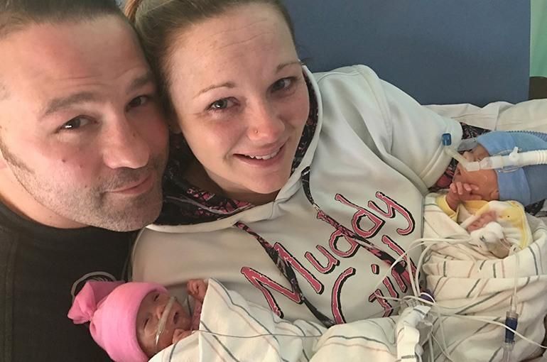 Jennifer and her husband smile a the camera while they hold their twins in the NICU for the first time.