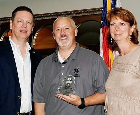 Jim Kuzmak stands with Bill and Laura Bachenberg, Camp Freedom Founders holding his “First Responder of the Year” award.