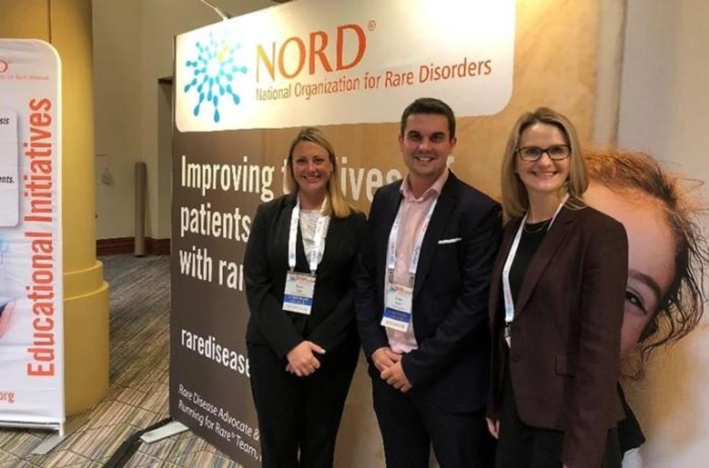 Two women and one man stand in front of a rare disease banner.