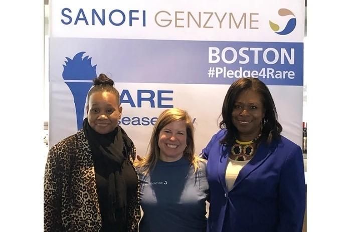 Lisa Schmitt and advocates from the Greater Boston Sickle Cell Disease Foundation stand in front of a rare disease day banner.