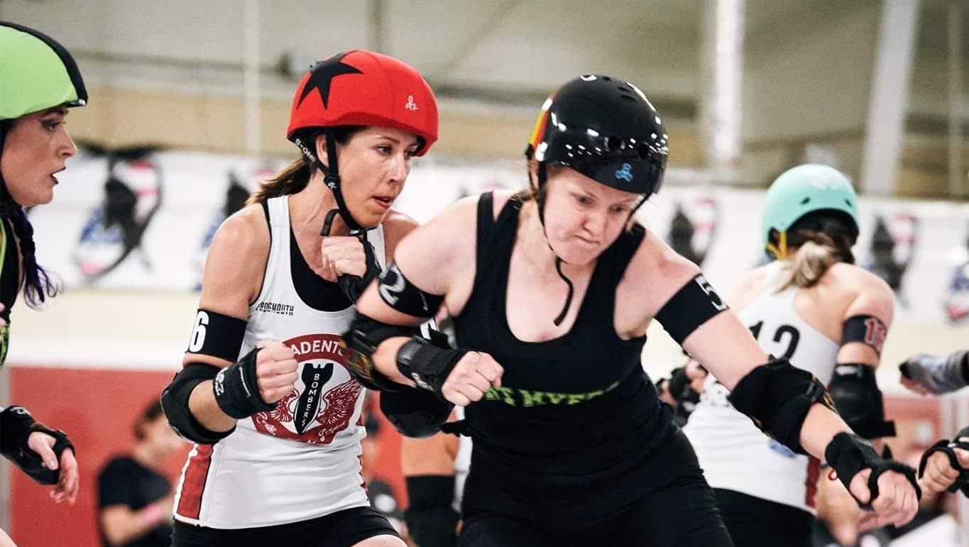 Melanie Stutts wears a helmet and elbow pads, pushing another woman out of the way during a roller derby match.