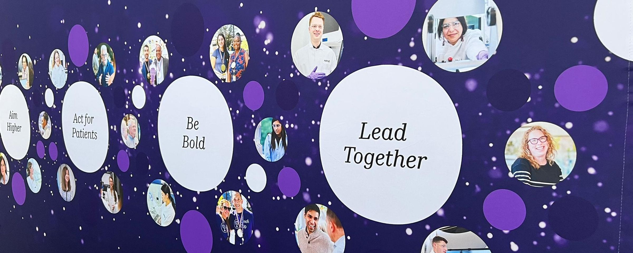 A purple-themed corporate image featuring diverse Sanofi team members in circular photographs with the text 'Lead Together' prominently displayed, alongside the values 'Aim Higher,' 'Act for Patients,' and 'Be Bold.’