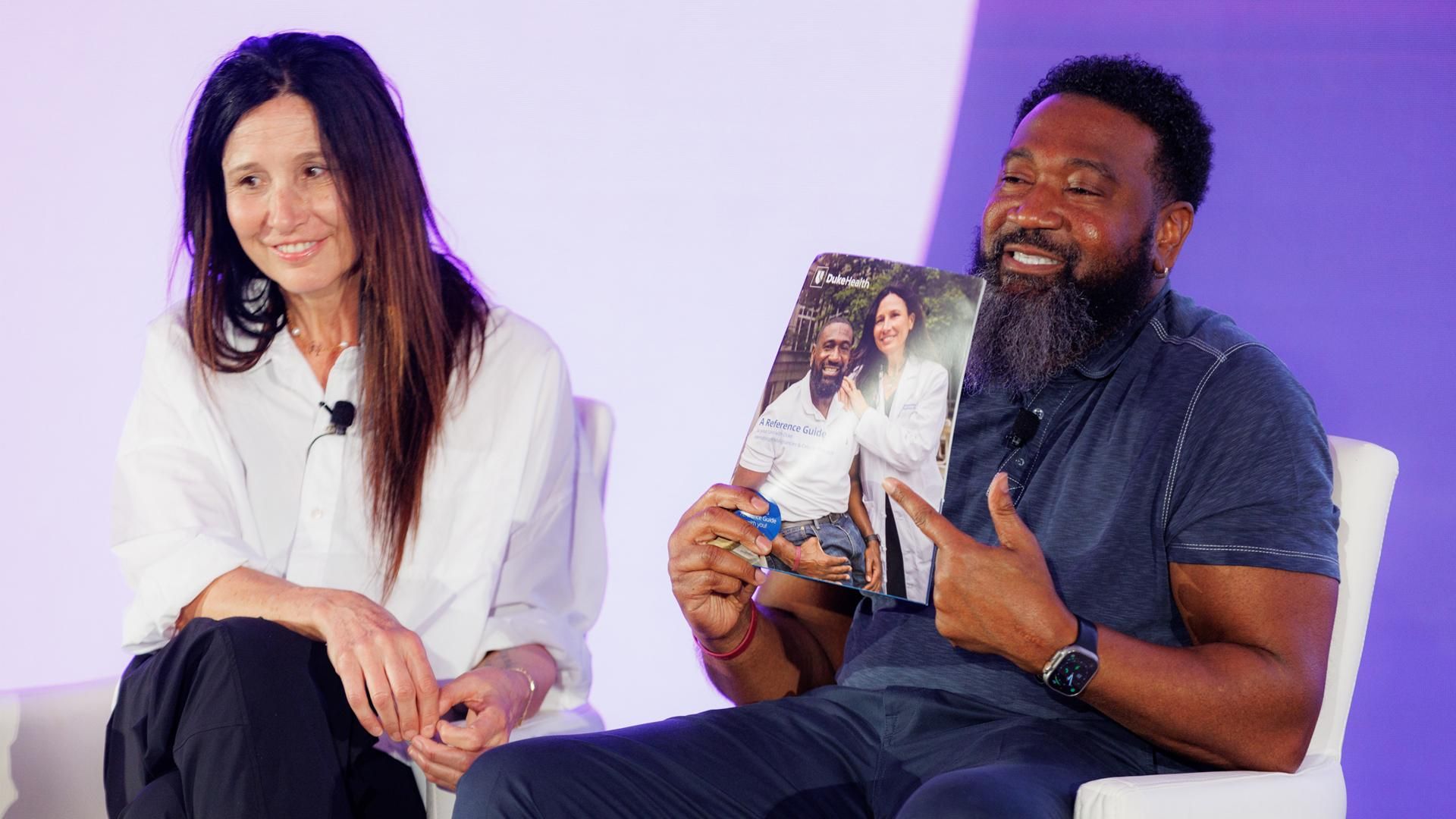 Thomas, living with multiple myeloma, sits next to his doctor, Dr. Cristina Gasparetto, while holding up a picture of the two of them in a magazine