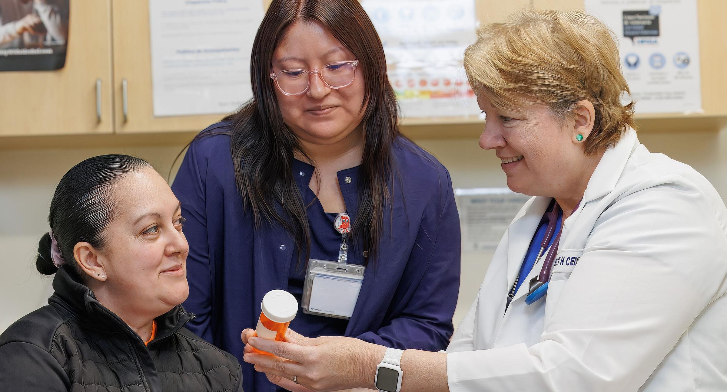 Two healthcare professionals in a clinic consulting with a patient about medication, one holding a prescription bottle while explaining treatment options.