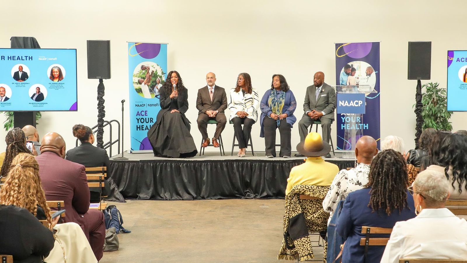 Five panelists speak to an audience from a stage.