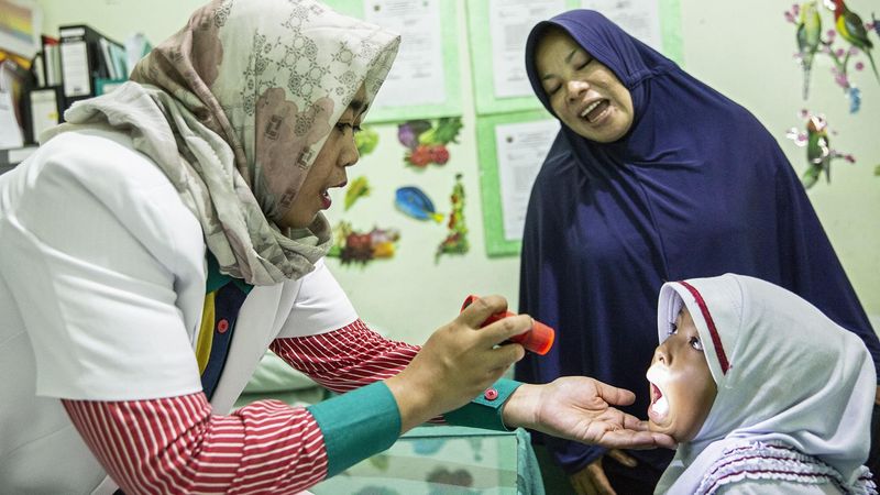 Dr Ariany Widiastuty shines a light in the mouth Salim while doing an examination, saying 'ahhhh' which the child mimics.