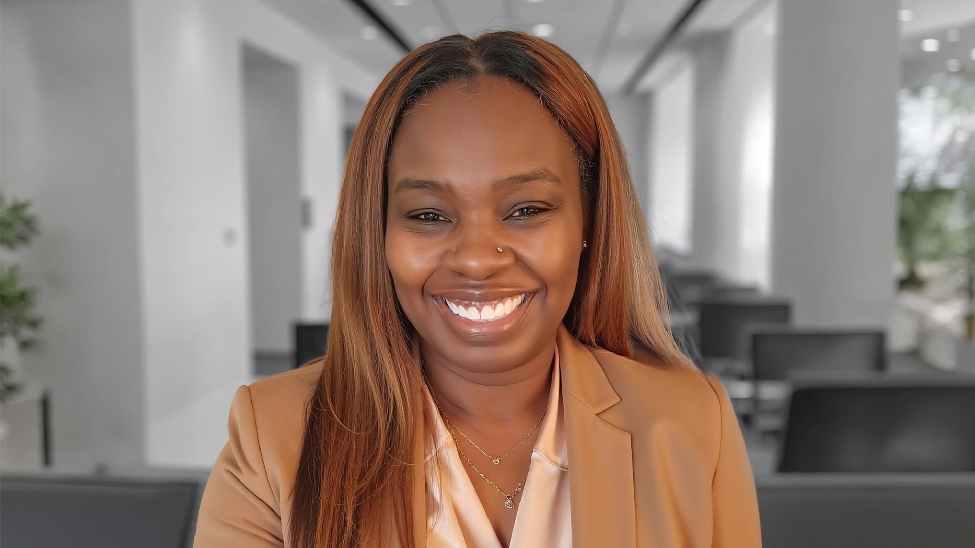Sanofi Inclusion Council member Tasha Wright, a black woman, smiles at the camera wearing a cream colored blouse and a dark beige blazer. 